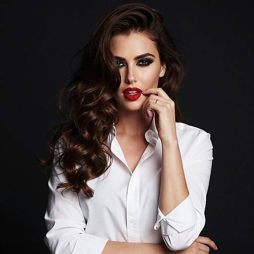 Photograph of a striking woman with long, wavy dark hair, wearing a white button-up shirt, biting a red lollipop, black background,