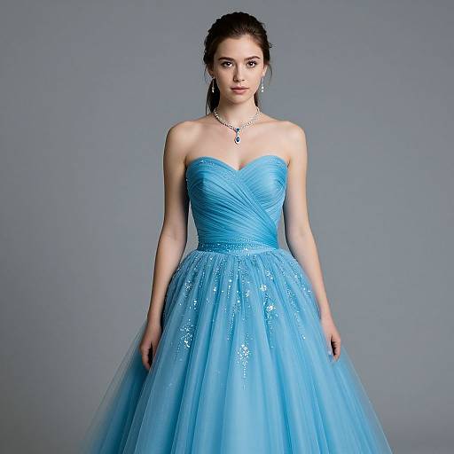 Photograph of a young woman with fair skin and dark hair in an elegant, strapless, sky-blue, sparkling tulle ball gown, standing against