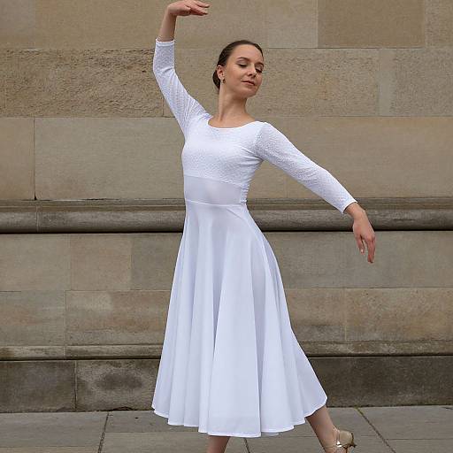 Photograph of a young woman with light skin and dark hair in a white, long-sleeve, lace-textured dress, dancing gracefully in front