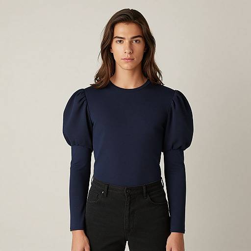 Photograph of a young man with long brown hair, wearing a navy blue, long-sleeved shirt with puffed sleeves, and black pants,