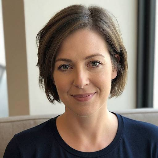 Photograph of a smiling woman with short brown hair, light skin, wearing a black shirt, seated against a softly lit background.