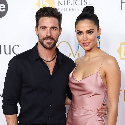 Photograph of a bearded man in a black shirt and a woman with dark hair in a bun, wearing a pink satin dress and blue earrings,