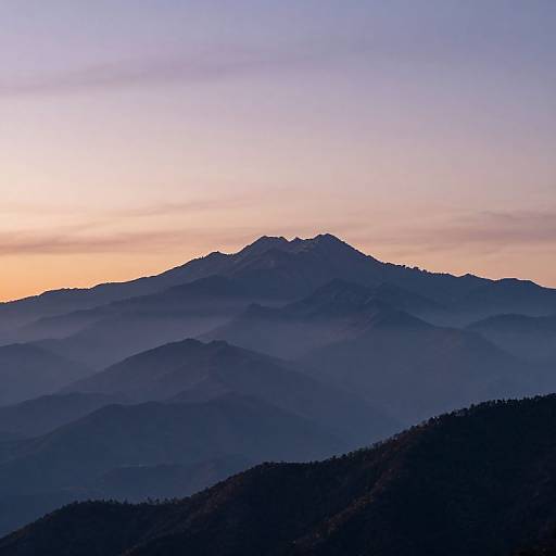 Photograph of a mountain range at dawn, with layers of blue and purple hills under a gradient sky from orange to purple.