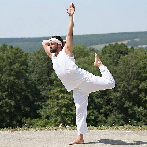 Photograph of a bearded man in white yoga outfit balancing on one leg, arms raised, wearing a white headband, outdoors with forested background