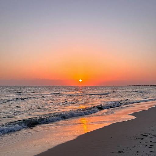 Photograph of a serene sunset over a calm ocean, with orange and pink hues in the sky, gentle waves, and a reflective wet shoreline.