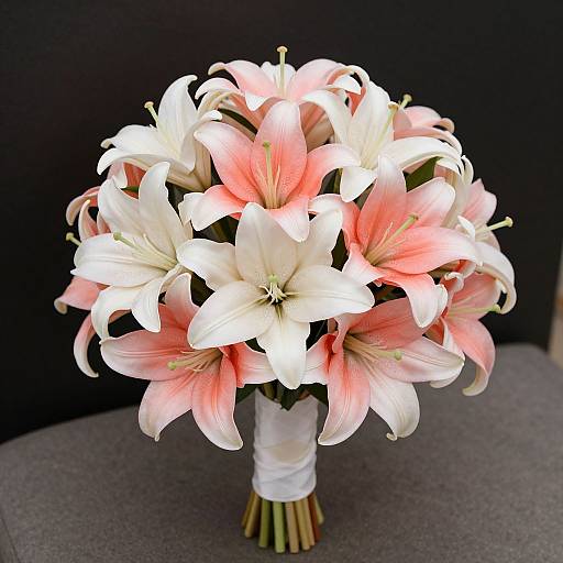 Photograph of a bouquet featuring large, pink and white lilies with vivid petals, wrapped in white ribbon, against a dark background.