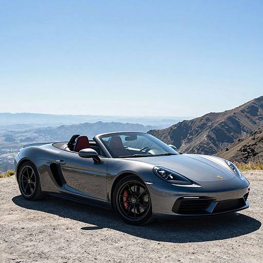 Photograph of a sleek, silver Porsche 911 convertible with black rims and red brake calipers, parked on a rocky mountain overlook under a clear blue