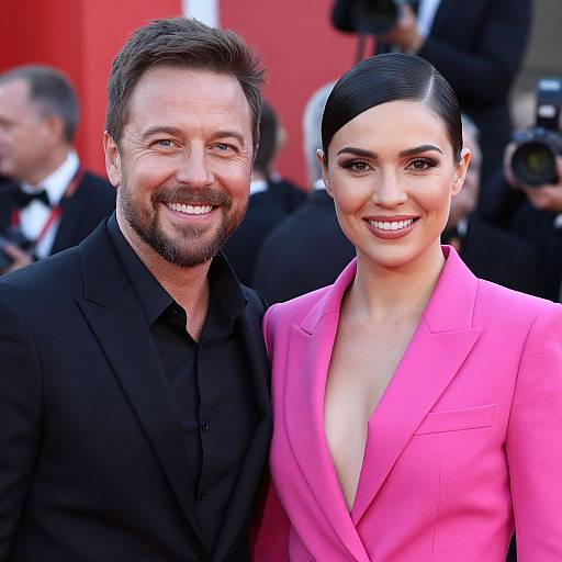 Photograph of a smiling, bearded man in a black suit and a woman with dark hair in a sleek bun, wearing a vibrant pink blazer
