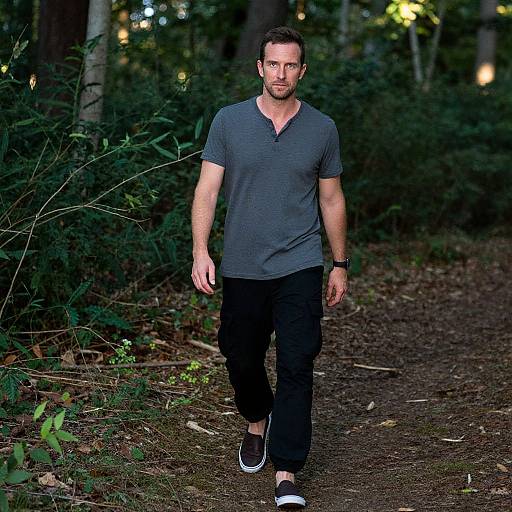 Photograph of a muscular, bearded man with short brown hair, wearing a dark gray V-neck tee, black pants, and black sneakers, walking