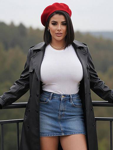 Photograph of a curvy woman with olive skin, dark hair, red beret, black coat, white top, and blue denim skirt, standing