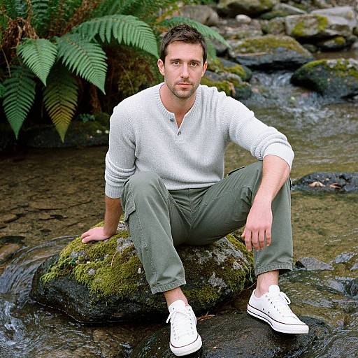 Photograph of a young man with short brown hair, light beard, wearing a white long-sleeve shirt, olive pants, and white sneakers,
