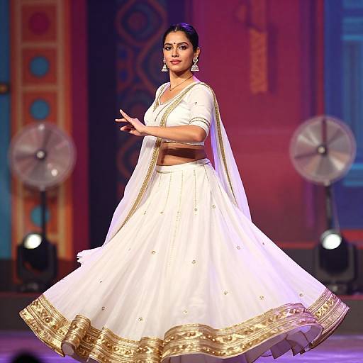 Photograph of a confident Indian woman in a white traditional lehenga with gold embroidery, mid-dance, against a colorful, illuminated stage backdrop.
