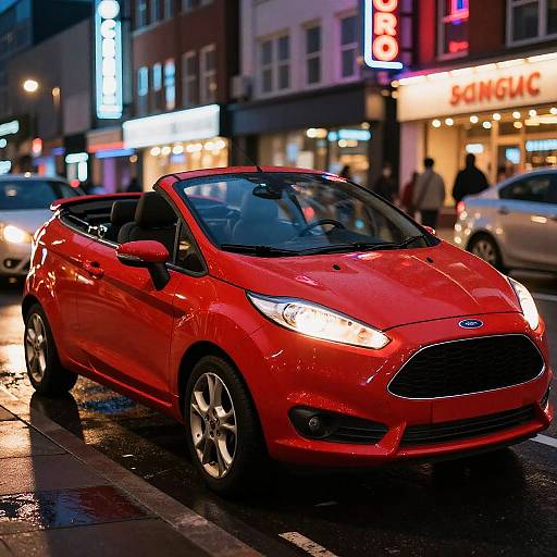 Photograph of a shiny red Ford Fiesta convertible parked on a wet, neon-lit urban street at night, with brightly lit storefronts in the background
