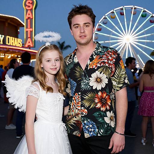 Photograph of a man in a floral shirt and a young girl in a white angel dress with halo headpiece, standing in front of a brightly lit