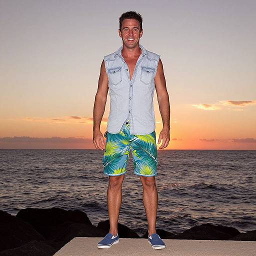 Photograph of a smiling, muscular man with short dark hair, wearing a sleeveless white vest, green and yellow shorts, and blue sneakers, standing