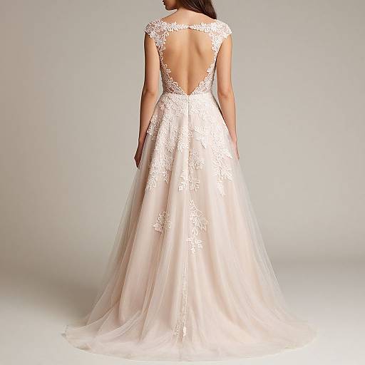 Photograph of a woman in an elegant, backless, white lace wedding gown with a sheer, flowing train, viewed from the back.