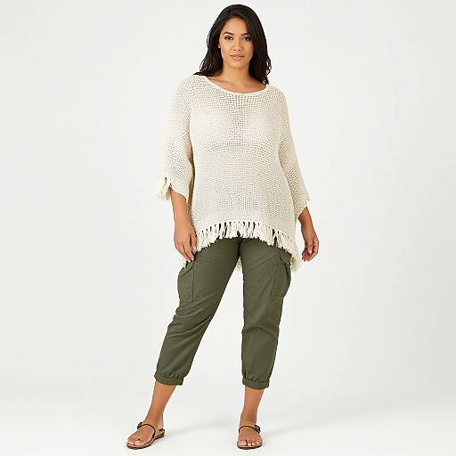 Photograph of a plus-size woman with long black hair, wearing a white crochet top, green capri pants, and black sandals, standing against a