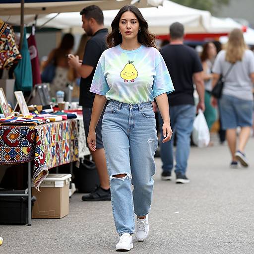 Photograph of a young woman with long dark hair, wearing a tie-dye shirt with a yellow pear print, light blue ripped jeans, and white