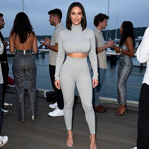 Photograph of a smiling woman with shoulder-length black hair in a light gray, long-sleeve, crop-top, and high-waisted pants