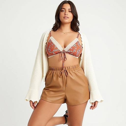 Photograph of a young woman with medium brown skin and dark wavy hair, wearing a red floral bralette, white knitted cardigan, and