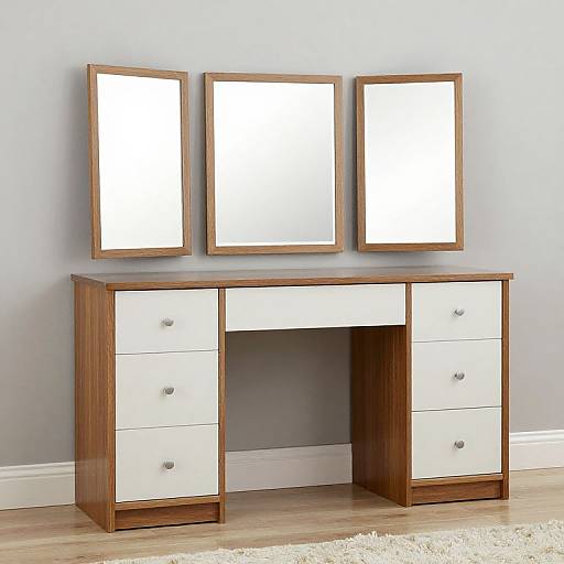 Photograph of a modern wooden vanity with three mirrored frames above, white drawers, and silver knobs, set against a light gray wall and wooden floor.