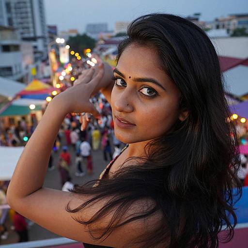 Photograph of a beautiful Indian woman with long black hair, dark eyes, and a bindi, posing with her hand raised, in a bustling evening