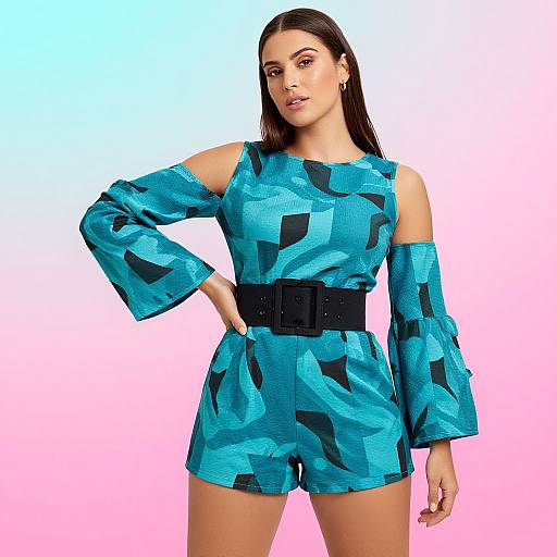 Photograph of a confident woman with long dark hair, wearing a blue geometric-patterned off-shoulder romper with black sleeves and belt, against
