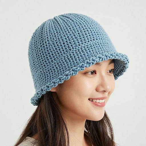 Photograph of a smiling young Asian woman with long black hair wearing a light blue, crocheted bucket hat against a white background.