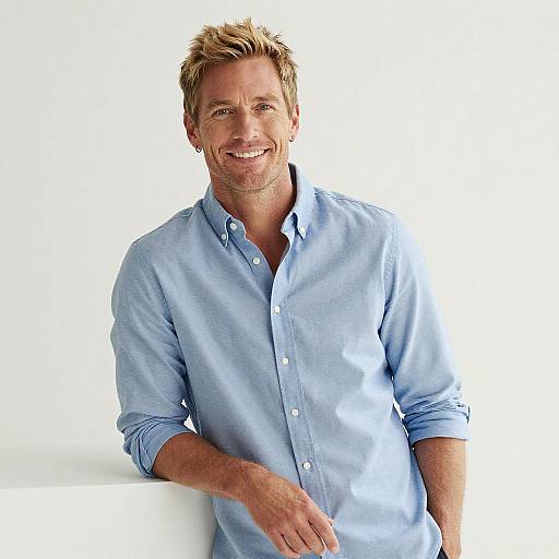 Photograph of a smiling, middle-aged man with blond hair, wearing a light blue, button-up shirt, against a plain white background.