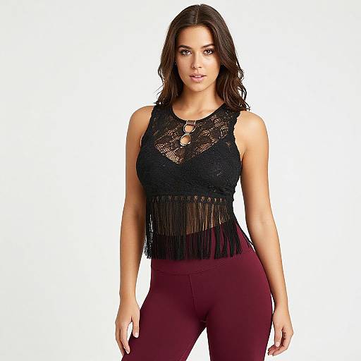 Photograph of a confident woman with wavy dark brown hair, wearing a black lace sleeveless top with fringe and maroon leggings, standing against a