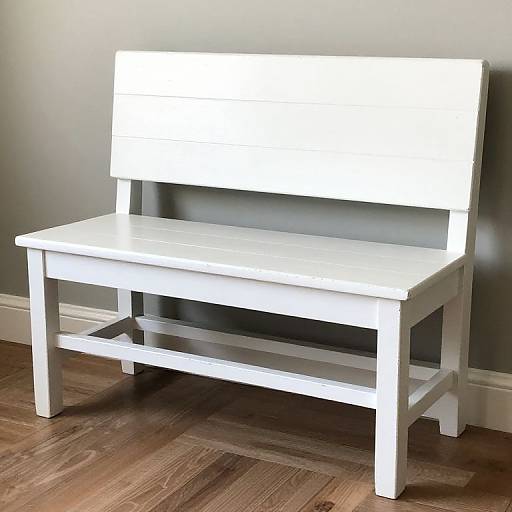Photograph of a white wooden bench with a backrest, set against a gray wall on a brown wooden floor.