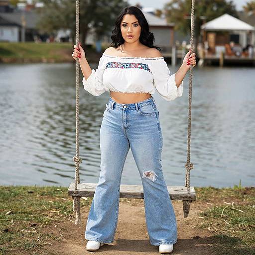 Photograph of a curvy woman with long black hair, wearing an off-shoulder white crop top and high-waisted blue jeans, sitting