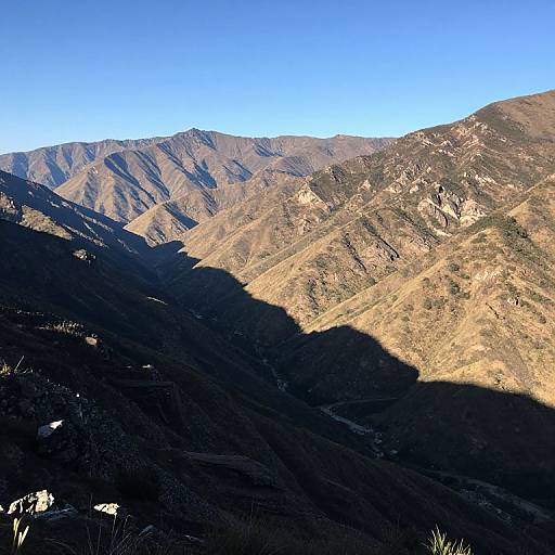 Photograph of sunlit, rugged mountain range with shadows cast on the lower slopes, under a clear, bright blue sky.