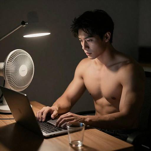 Shirtless Man Working on Laptop at Desk