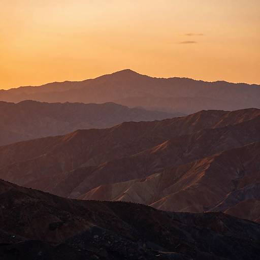 Photograph of a sunset over layered mountain ranges, with a gradient from dark purple peaks in the foreground to a bright orange sky in the background.