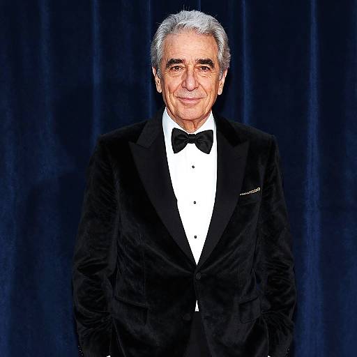 Photograph of an elderly man with gray hair, wearing a black tuxedo with a bow tie, white shirt, and black velvet lapel,