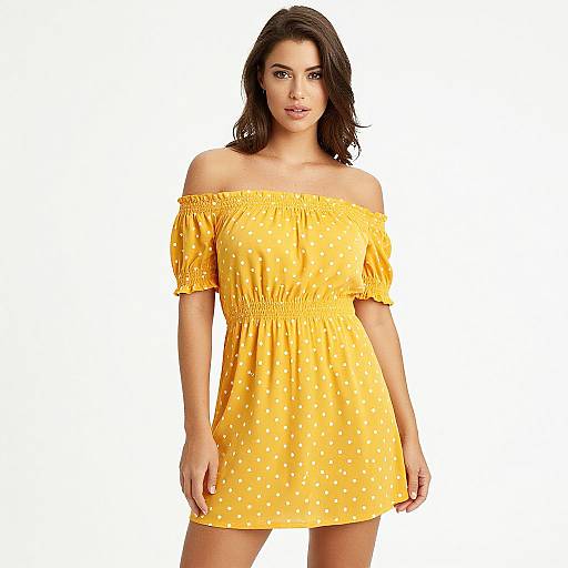 Photograph of a young woman with wavy brown hair wearing an off-shoulder, yellow polka dot dress against a white background.