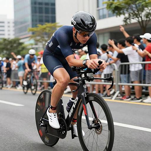 Photograph of a focused male cyclist in a navy-blue outfit, black helmet, and white shoes, riding a black road bike during a city race,