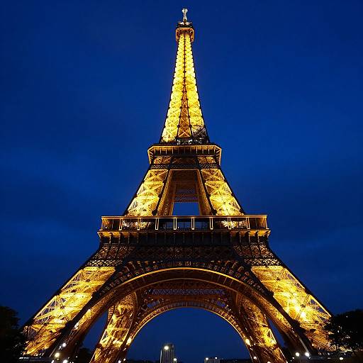 Photograph of the Eiffel Tower illuminated in golden lights against a deep blue evening sky, showcasing its iconic architectural structure.