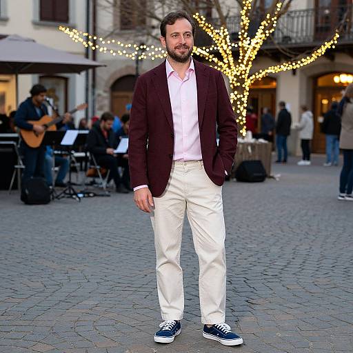 Photograph of a bearded man with short dark hair, wearing a brown blazer, white shirt, beige pants, and black sneakers, walking in