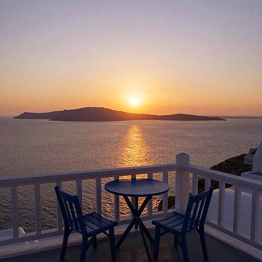 Photograph of a serene sunset over a calm ocean, with a small blue wooden table and two matching chairs on a white-railed balcony.