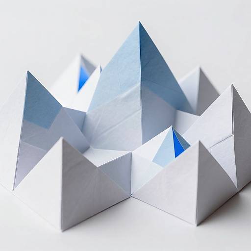 Photograph of a modern, abstract paper sculpture with sharp, angular, reflective silver and blue geometric shapes on a white background.