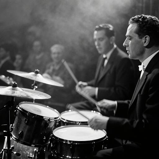 Black-and-white photograph of four male jazz musicians in suits, playing drums and percussion, with a smoky background. Foreground drummer in sharp profile.