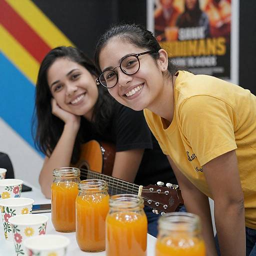Two Women Smiling with Orange Drinks and Guitar