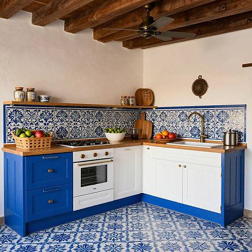 Photograph of a rustic kitchen with blue cabinets, white countertops, blue patterned tiles, wooden ceiling beams, and blue patterned floor tiles.