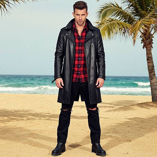 Photograph of a muscular, dark-haired man in a black leather coat, red plaid shirt, black pants, and boots, standing on a sunny