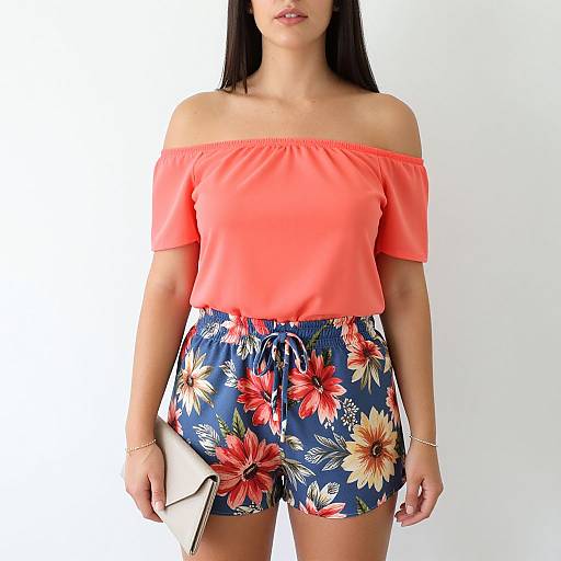 Photograph of a woman with long black hair wearing an off-shoulder coral top and floral blue shorts, holding a white clutch.
