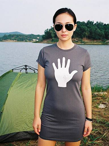 Photograph of a woman with dark hair, sunglasses, and a gray t-shirt with a white handprint, standing in front of a green camping tent