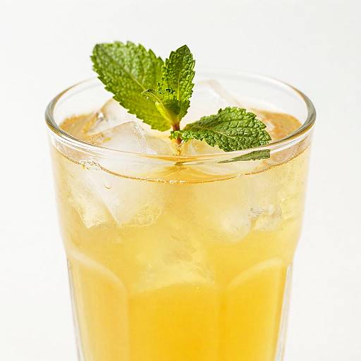 Photograph of a glass of orange-colored drink with ice cubes and two fresh green mint leaves on a white background.