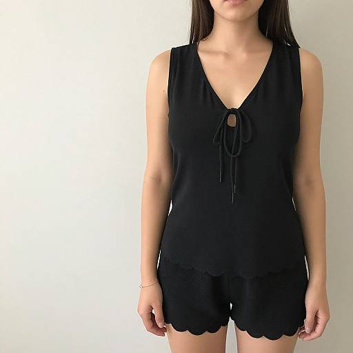 Photograph of an Asian woman with long black hair, wearing a sleeveless black V-neck top with a bow tie and scalloped black shorts,